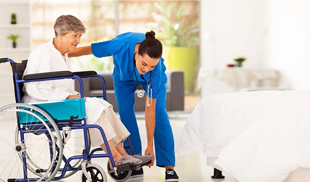 Nurse kneeling down near to assist older woman in a wheelchair 