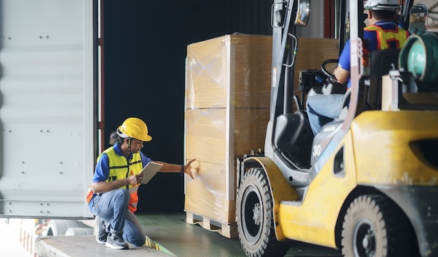 Technician kneeling down near crane to secure packages using the MobiWork DSD/supply chain/milk run services software solution