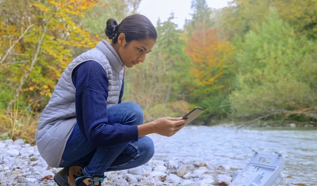 Woman kneeling down near creek taking metrics using the MobiWork environmental services software solution