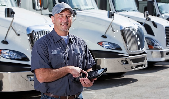 Technician standing in front of semi-truck holding tablet using the MobiWork fleet management & services software solution