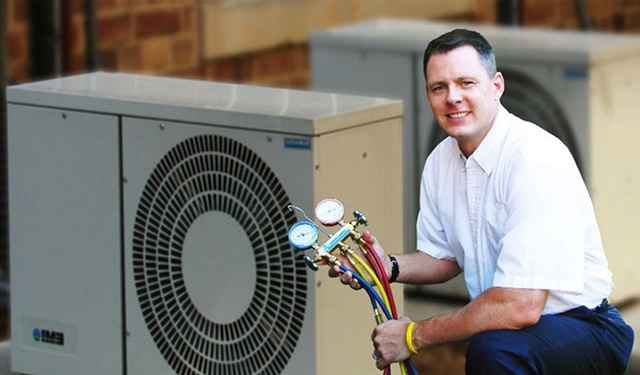 Technician kneeling down near HVAC units on roof using the MobiWork HVAC services software solution