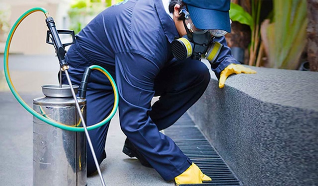 Technician kneeling down outside applying pesticides to the surrounding area using the MobiWork pest control services software solution